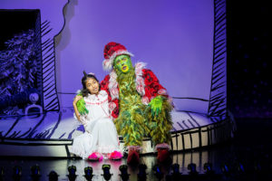Cindy-Lou Who and The Grinch sit midstage as they sing.