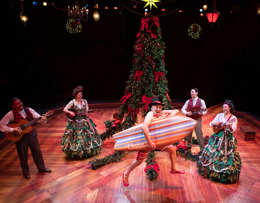 Cast sings onstage before a Christmas tree. Ebenezer is in his bathing suit with a surfboard.