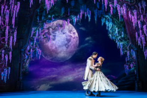 Hans and Elsa dance onstage framed by a moon and trees.