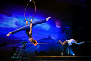 Two aerialists are suspended - one on a hoop and another on a cable,