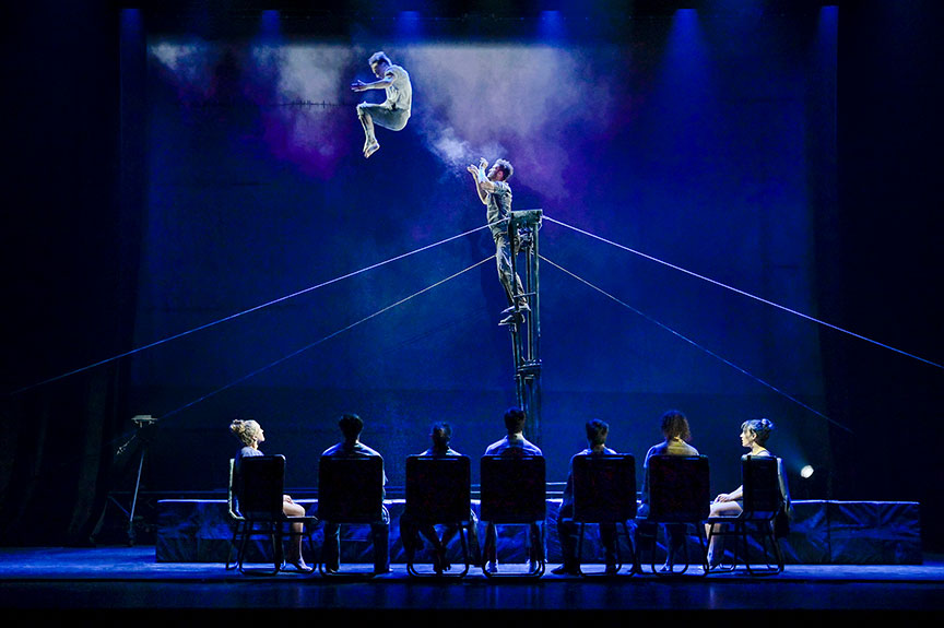 Acrobats fly through the air while the actors look on.