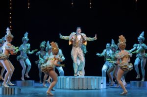 The cast dances on large coins during "We're in the Money."